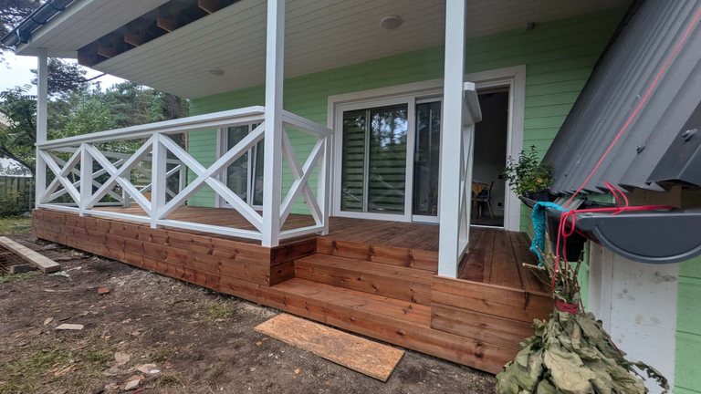 Dark timber deck with white X railing and steps by a light-green house